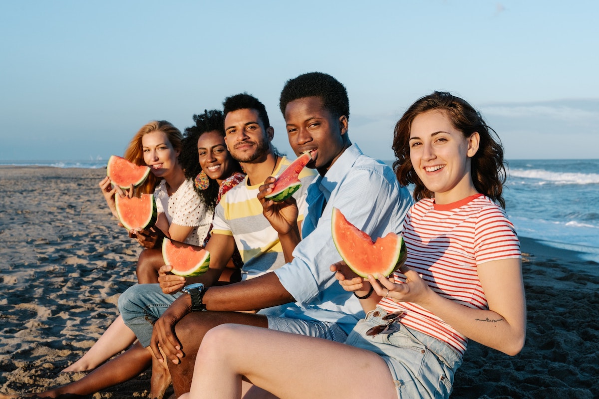 image of people in a happy and engaging group photo, eating watermelons on the beach. it's a good example of what could be UGC