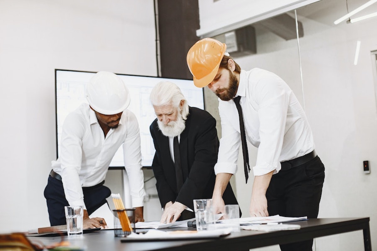 image of 3 mean in suits and hardhats bent over a table working