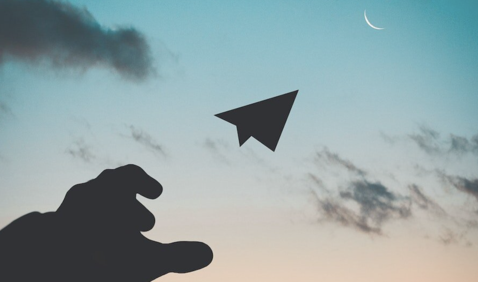 decorative image of a shadowed hand throwing a paper airplane into a sunsetting sky with a crescent moon