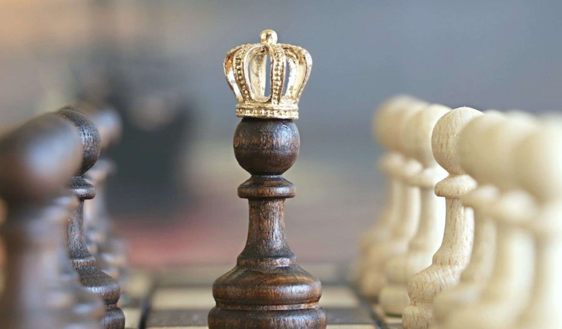 image of chess pieces, one of which has a gold crown on top